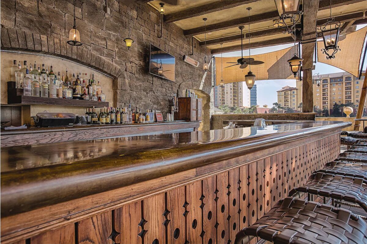 A bar area with a stone wall, wooden bar counter, and hanging lights.