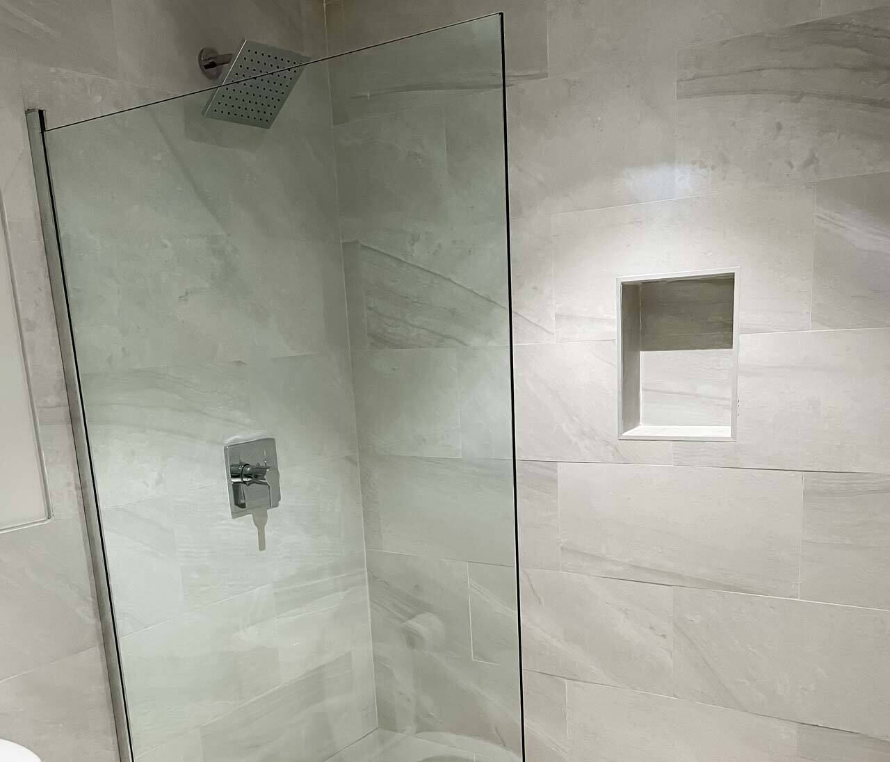 A glass-enclosed shower with a handheld showerhead and a control panel.
