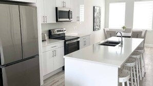 A modern kitchen with white cabinetry, stainless steel appliances, and a central island with bar stools. - The Pelican Villa (Nassau)