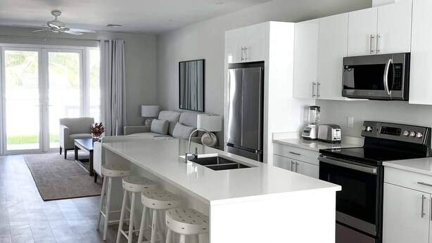 A modern kitchen with a central island, stainless steel appliances, and white cabinetry. - The Pelican Villa (Nassau)