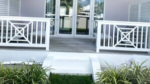 A white building with a covered porch, glass doors, and a white railing. - The Pelican Villa (Nassau)