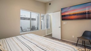 Un dormitorio con una cama grande, un televisor en la pared y una ventana con persianas.