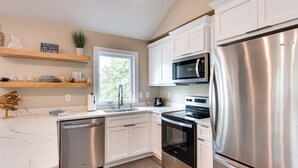 A modern kitchen with white cabinets, stainless steel appliances, and wooden shelves. - Lakefront Home w/ Private Dock in Sunrise Beach! (Sunrise Beach)