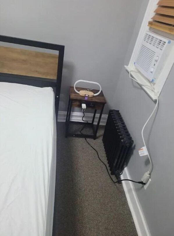 Ein kleines Schlafzimmer mit einem Bett, einem Nachttisch mit Lampe, einem Heizkörper und einer Wandheizung.