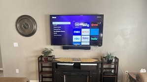 Ein Wohnzimmer mit Flachbildfernseher an der Wand, einem Kamin und zwei Beistelltischen mit Pflanzen.