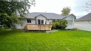 Ein Haus mit umzäunter Rückseite, einer Holzterrasse und einem gepflegten Rasen.