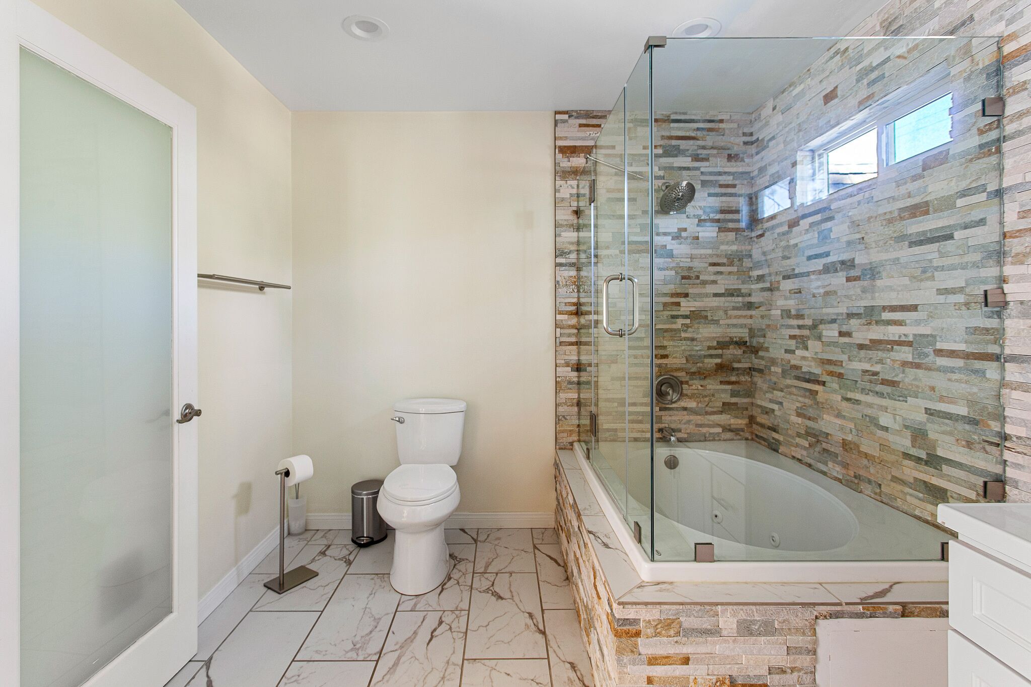 Een moderne badkamer met een douchecabine van glas, een vloer van marmer en een toilet.