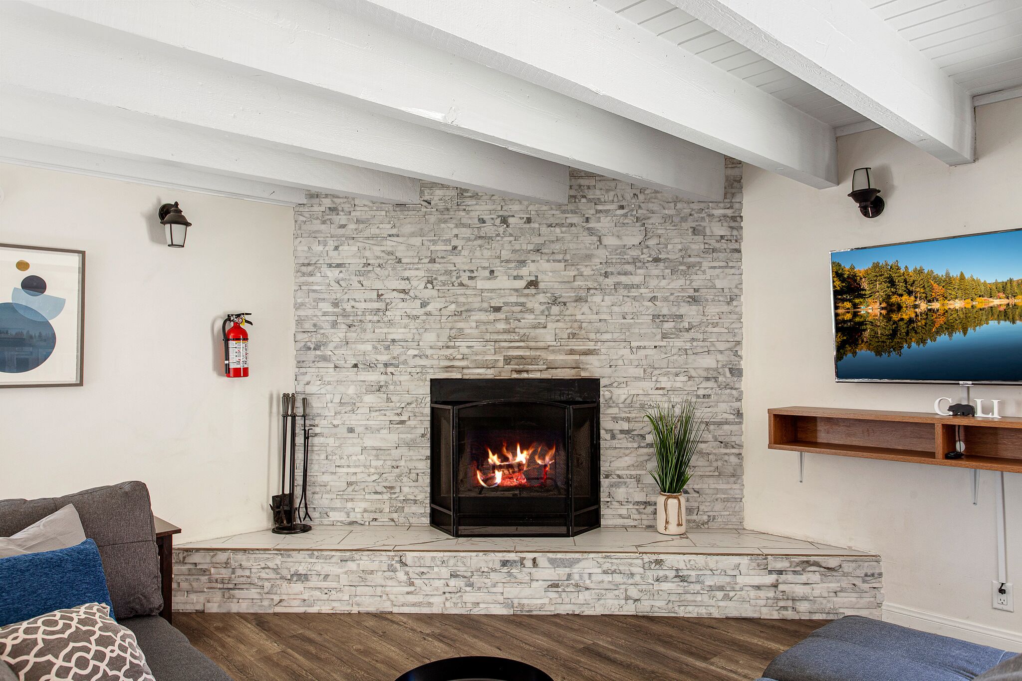 Una sala de estar con chimenea de piedra, televisor montado y extintor.