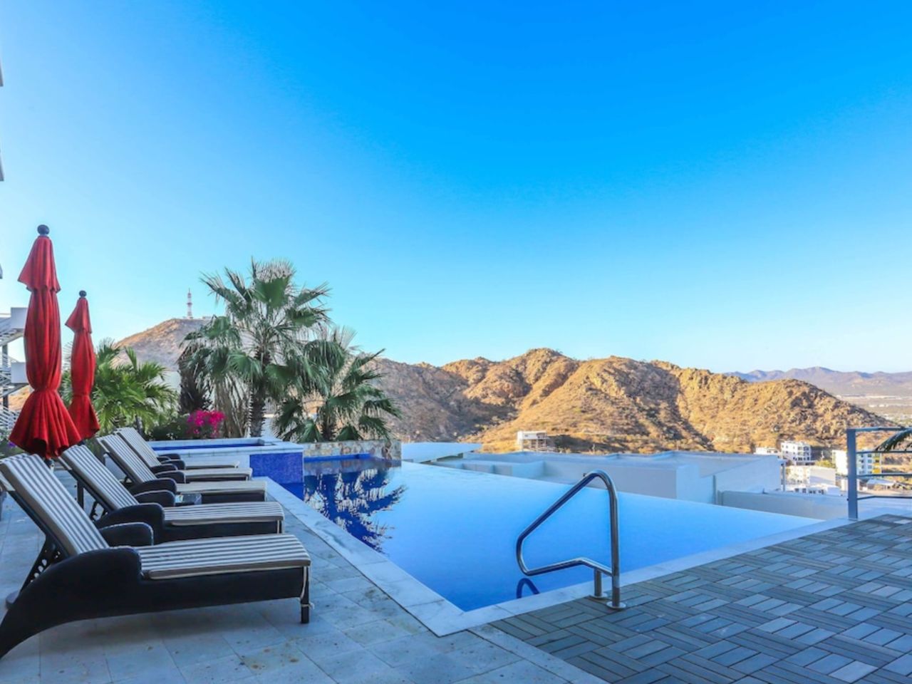 A rooftop infinity pool with lounge chairs and umbrellas, overlooking a mountainous landscape.
