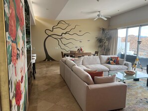 A living room with a sectional sofa, a glass coffee table, and a wall mural.