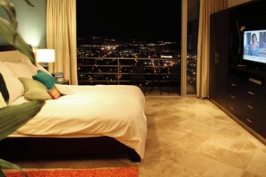A hotel room with a bed, a television, and a view of the city at night.