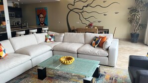 Uma sala de estar moderna com um sofá de canto, uma mesa de centro de vidro e uma área de jantar com mesa de vime.