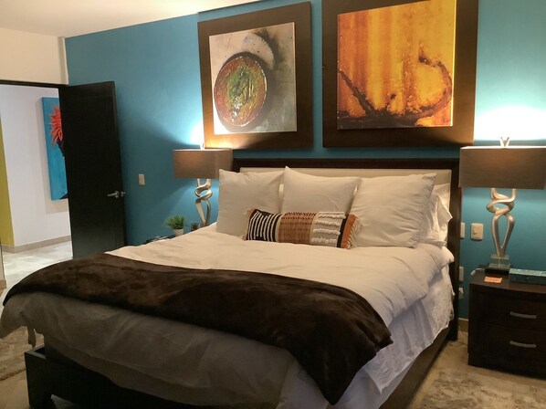 A hotel room with a bed, two bedside tables, a nightstand, and artwork on the walls.