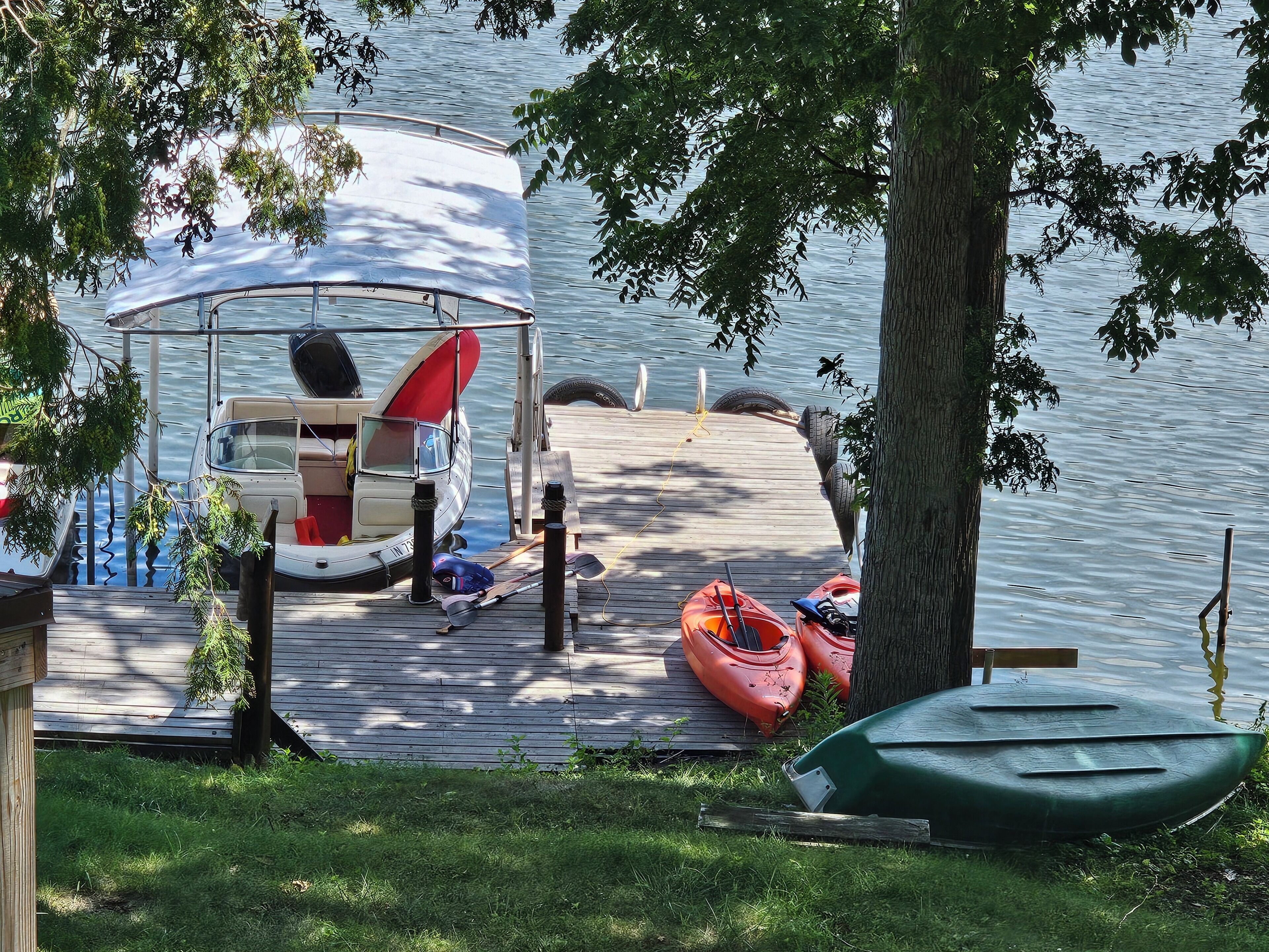 A dock with a covered boat, kayaks, and a green canoe.