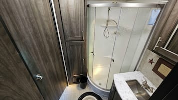 A bathroom with a shower, toilet, sink, and a mirror.