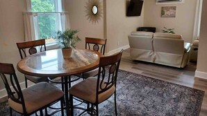 Un coin repas avec une table ronde et des chaises, une plante en pot et un canapé à l’arrière-plan.