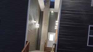 Un escalier menant à un bâtiment de couleur sombre, doté d’une porte et d’une petite fenêtre.