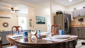 A dining area with a round table, chairs, and a ceiling fan. There is a kitchen area with a refrigerator and cabinets in the background. - Coastal Purple: Minutes to Cedar Point & Sports Complex! Sleeps 9 (Sandusky)