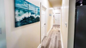 A hallway with a wooden floor, a large ocean-themed painting on the wall, and a refrigerator on the right. - Coastal Purple: Minutes to Cedar Point & Sports Complex! Sleeps 9 (Sandusky)