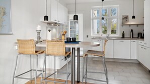 Une cuisine moderne avec des meubles blancs, une table de salle à manger ronde et trois tabourets de bar en osier.