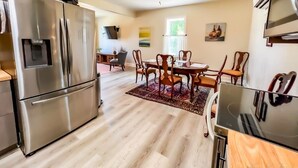 Una cucina moderna con elettrodomestici in acciaio inossidabile, un'area pranzo con sedie in legno e una ventola a soffitto.