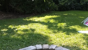 Un focolare in pietra circolare con un bordo in mattoni, circondato da erba e alberi.