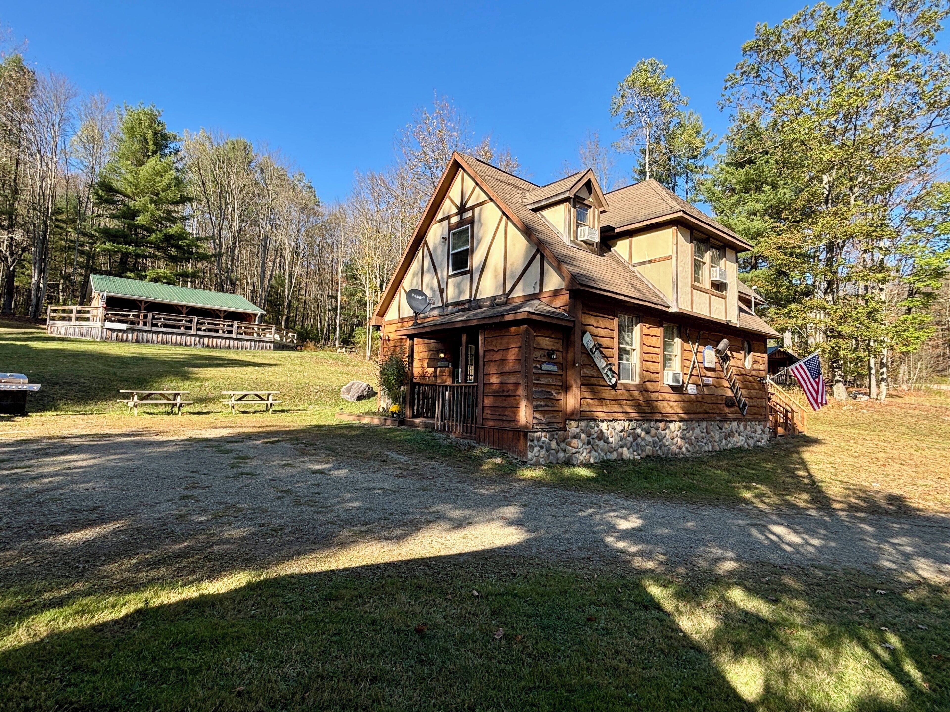 A log cabin with a stone foundation, a picnic area with benches, and an American flag.