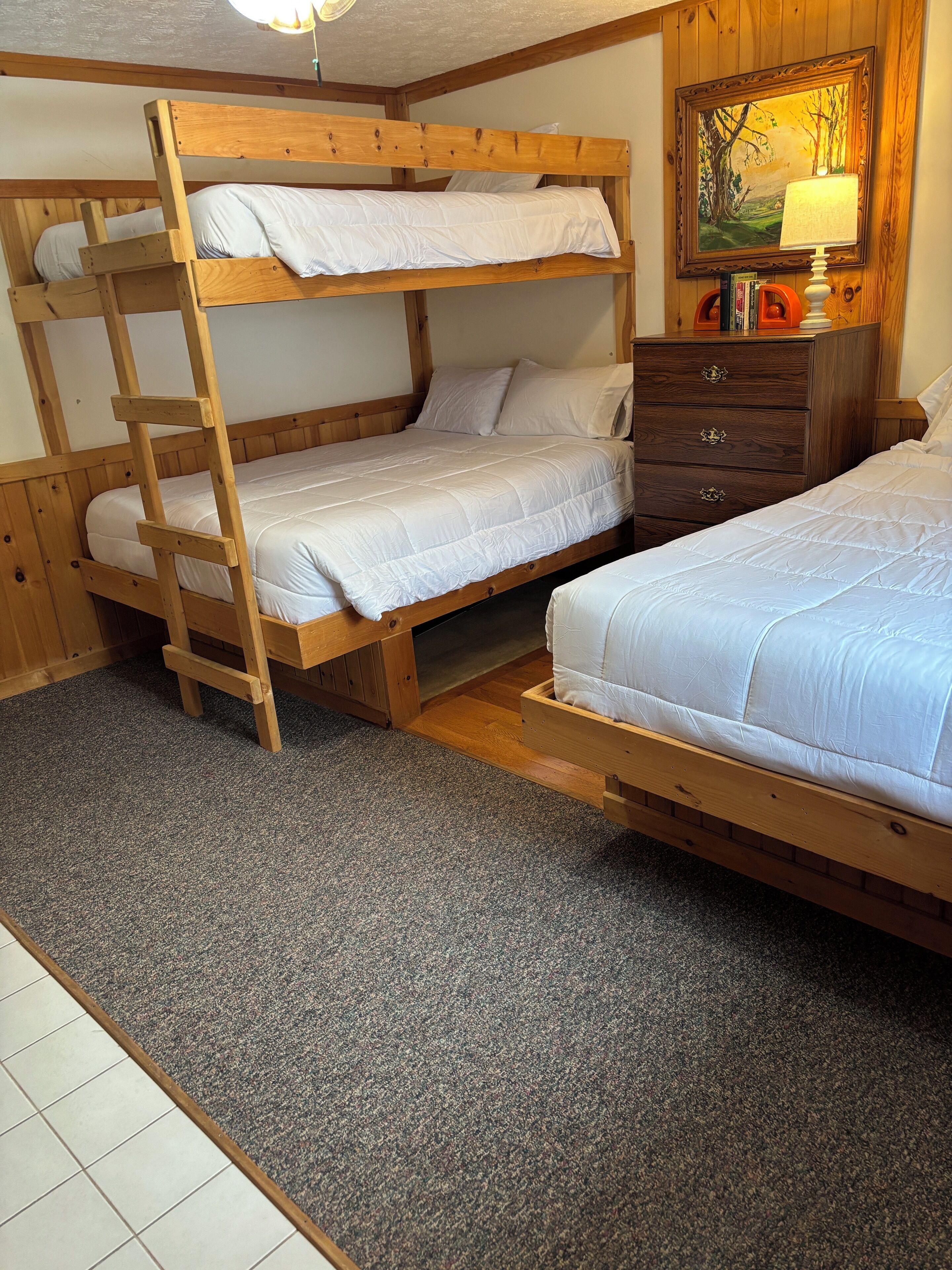 A bunk bed room with a ladder, a dresser, and a painting on the wall.