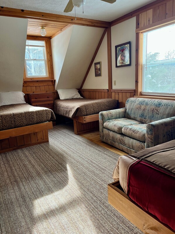 Un dormitorio acogedor en el ático, con techo inclinado, vigas de madera, un ventanal y vistas al exterior.