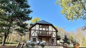 A two-story lodge with a stone foundation, a balcony, and a stone staircase leading to the entrance. - HUGE 3 Home Lodge For Large Groups, Lots of Space For Entertaining & Privacy! (Great Valley)