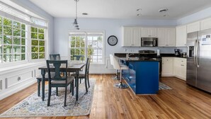 A kitchen with white cabinets, a blue island, a stainless steel refrigerator, and a dining area with a table and chairs. - Lake Carolina Condo | 3BR 2.5BA (Columbia)
