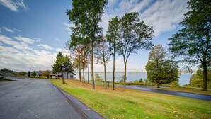 Rua residencial com casas, área gramada e um lago ao fundo.