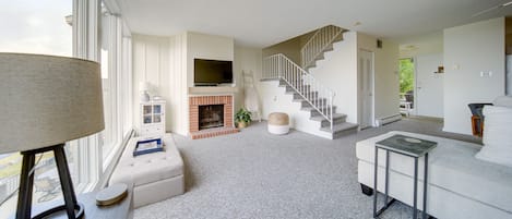 A modern living room with a fireplace, a staircase, and a large window.
