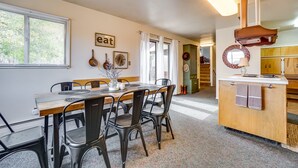 Un coin repas avec une table et des chaises en bois, une cuisine avec un comptoir et des placards, et une fenêtre avec des stores.