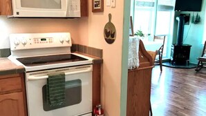 A kitchen with a white stove, wooden cabinets, and a microwave above it. - Millers' Misfit Farm (Prineville)
