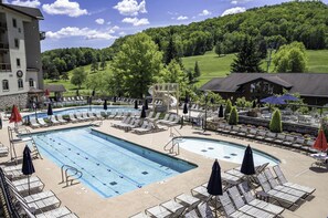 A pool area with lounge chairs, a water slide, and a view of a green landscape.