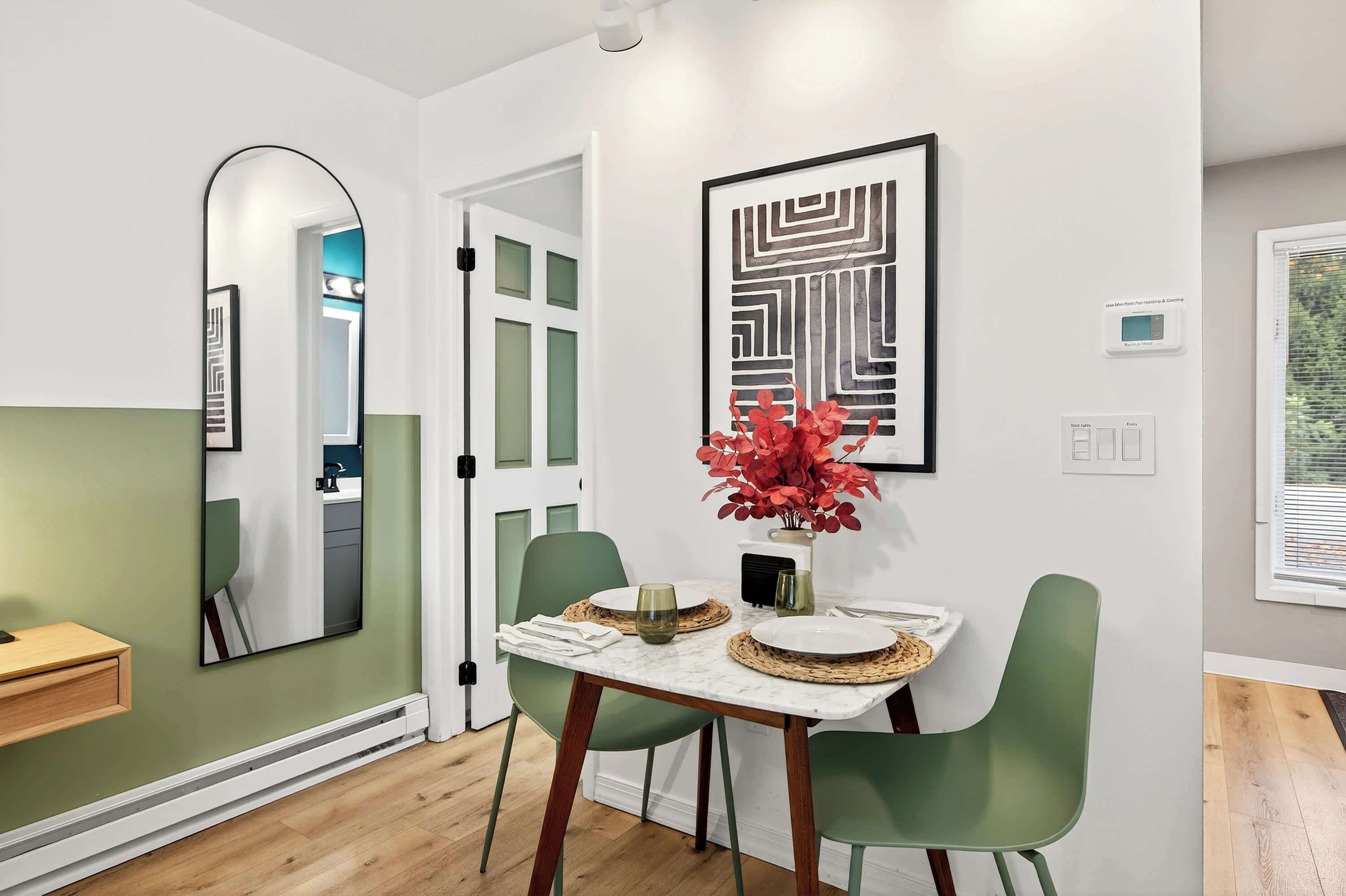 A dining area with a table, chairs, a mirror, and a wall-mounted thermostat.