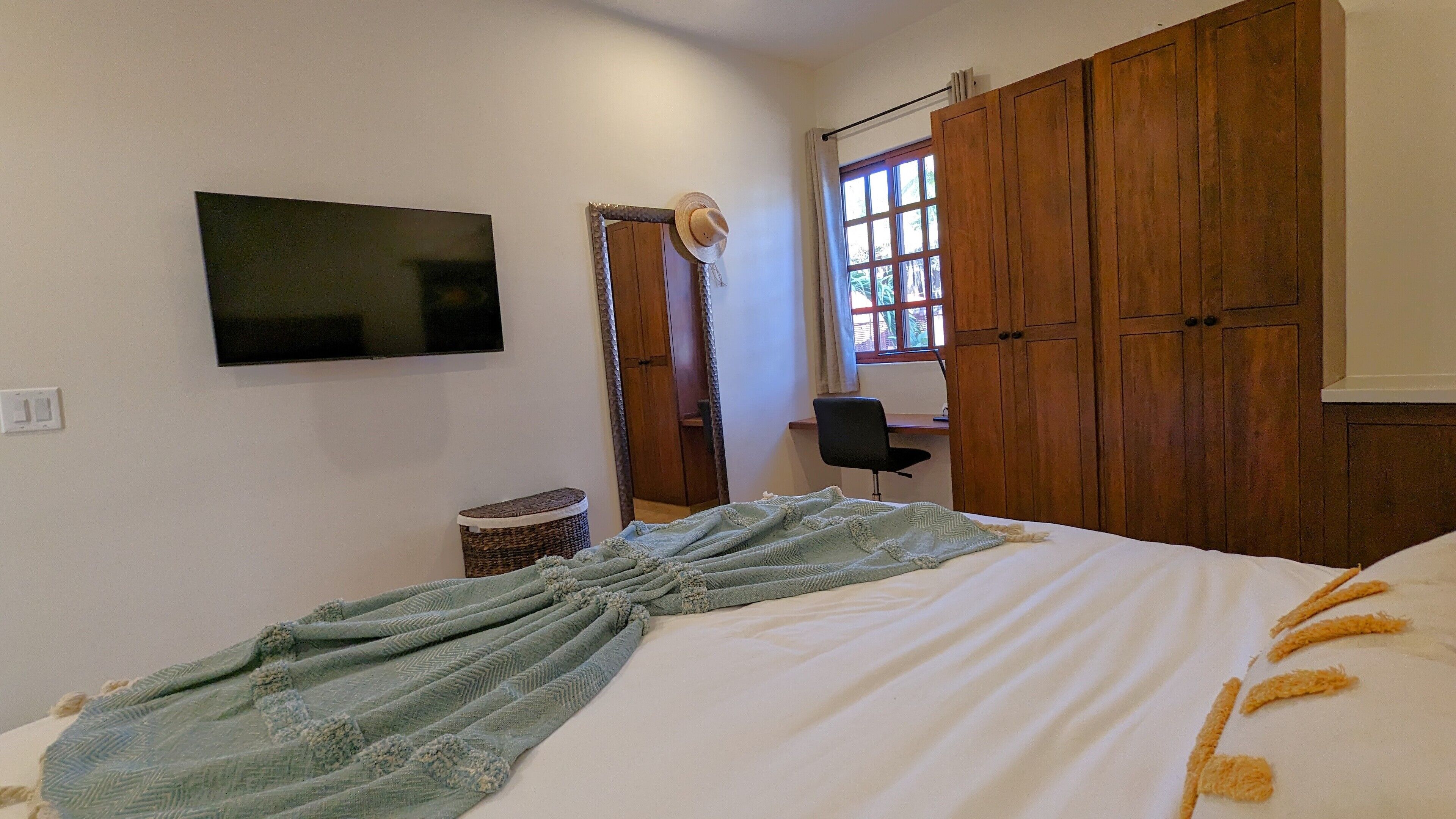 Un dormitorio con cama, televisor, armario, escritorio y silla.
