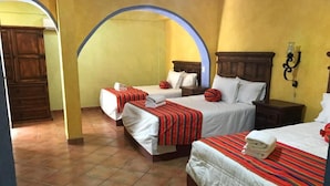 Une chambre d’hôtel avec trois lits, chacun recouvert d’une couvre-lit à rayures rouges et doté de draps blancs. Il y a deux tables de chevet avec des lampes, et la chambre a un sol carrelé et des murs jaunes.