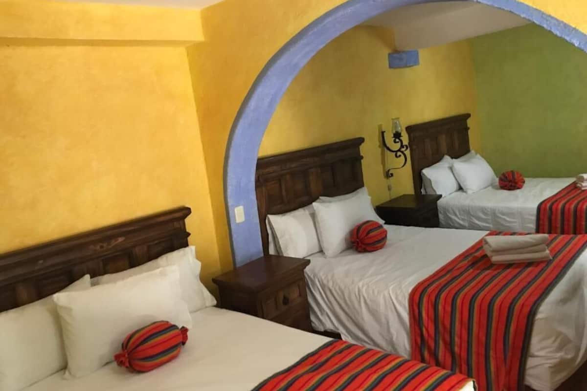 Quarto de hotel com duas camas, uma cabeceira de madeira e um arco azul.