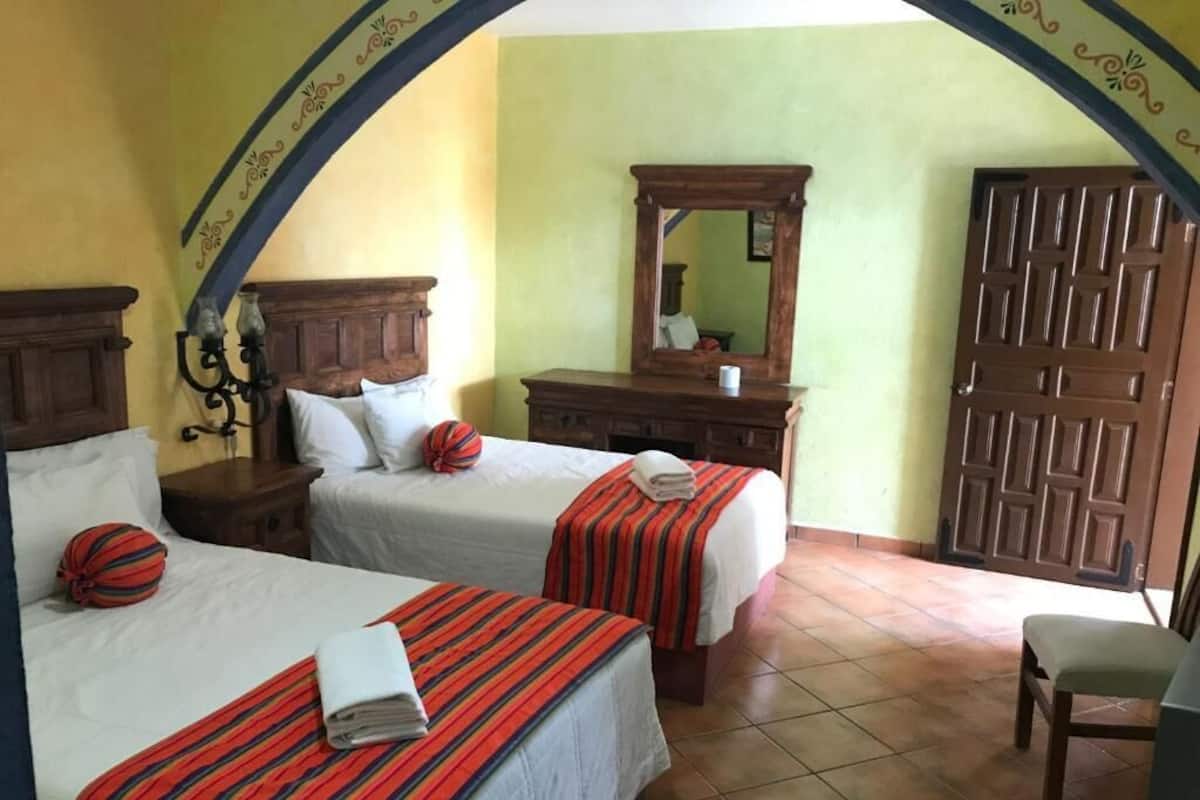 Quarto de hotel com duas camas, uma cômoda de madeira, um espelho e uma porta.