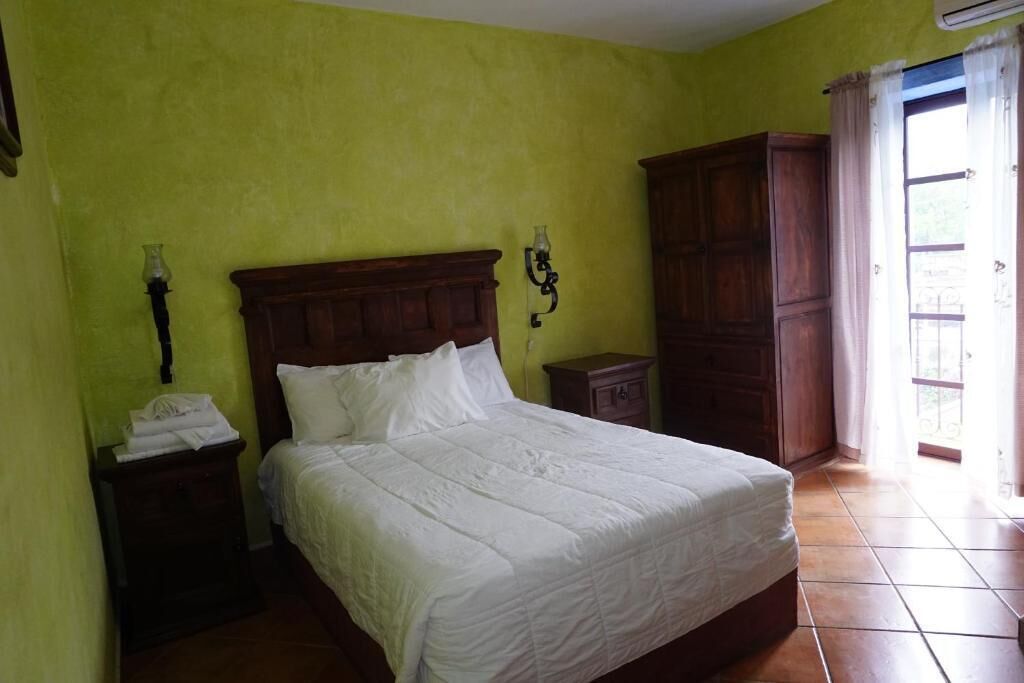 A room with a bed, a nightstand, a wardrobe, and a window with curtains.