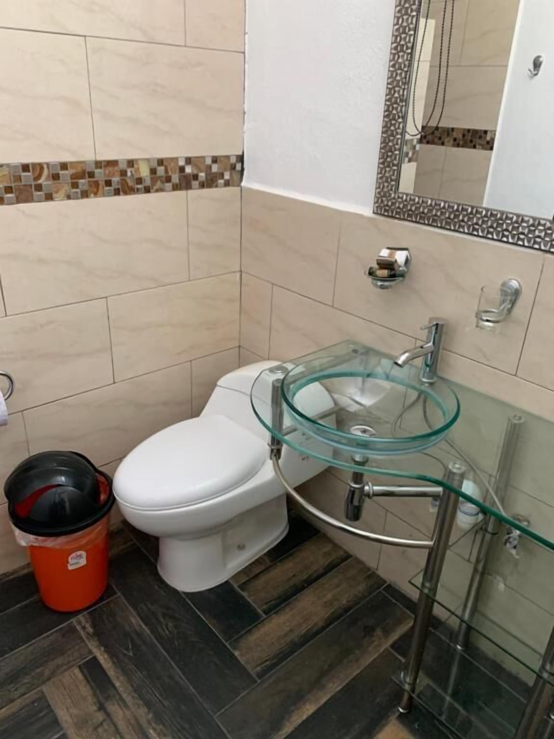 Un baño con inodoro, lavamanos de vidrio y suelo de baldosas.