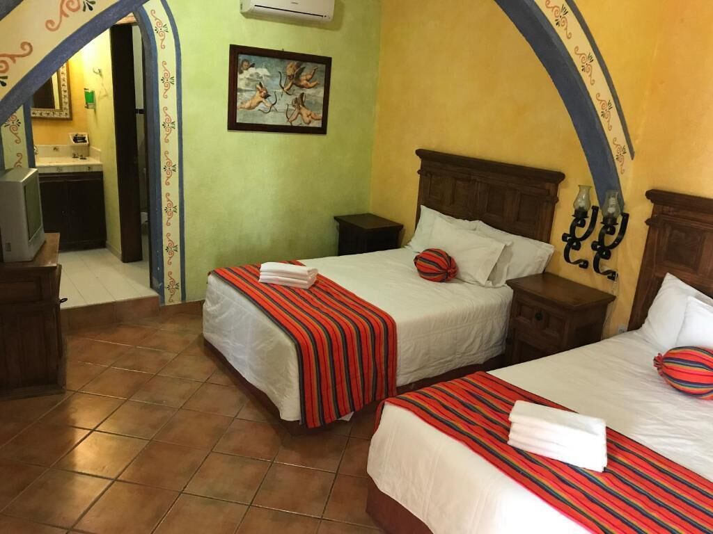 A hotel room with two beds, a small desk, a chair, a nightstand, and a wall-mounted air conditioner.