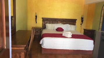 Una habitación de hotel con una cama de madera, una mesita de noche, un escritorio y un televisor.
