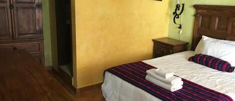 A hotel room with a bed, a nightstand, a wooden wardrobe, and a wall-mounted lamp.
