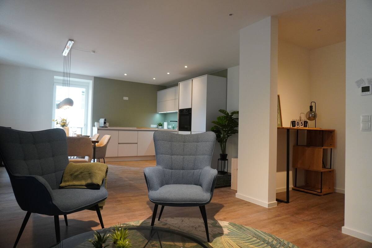 Ein modernes Wohnzimmer mit zwei grauen Sesseln, einem Couchtisch und einem Holzregal.