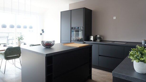 A modern kitchen with a central island, black cabinetry, and a large window providing natural light. - Sleepwell Apartment - Ehrensteinsuite (Leipzig)