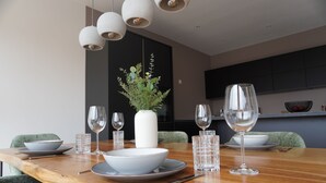A modern dining area with a wooden table set for a meal, a vase with greenery, and a flat-screen TV mounted on the wall. - Sleepwell Apartment - Ehrensteinsuite (Leipzig)