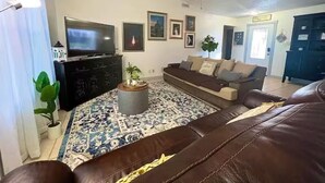 A living room with a brown leather sofa, a television, a ceiling fan, and a patterned rug. - Casa Santa Clara with Swimming Pool near Golf Country Clubs (Brownsville)